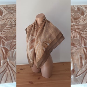 May include: A brown and beige scarf with a floral pattern. The scarf is folded and draped over a mannequin.
