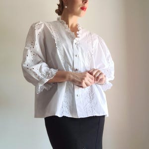 Puede incluir: Blusa blanca con detalles de calados y encaje. La blusa presenta un cuello y mangas con volantes, con un dise&ntilde;o cl&aacute;sico y elegante. Las mangas son de tres cuartos. La blusa se combina con una falda l&aacute;piz negra.
