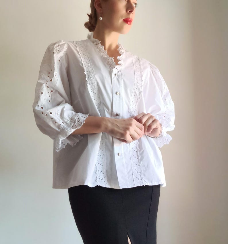 Puede incluir: Blusa blanca con detalles de calados y encaje. La blusa presenta un cuello y mangas con volantes, con un dise&ntilde;o cl&aacute;sico y elegante. Las mangas son de tres cuartos. La blusa se combina con una falda l&aacute;piz negra.