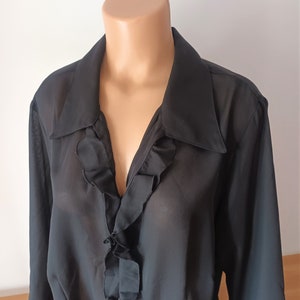 May include: A black sheer blouse with a ruffled neckline and long sleeves.