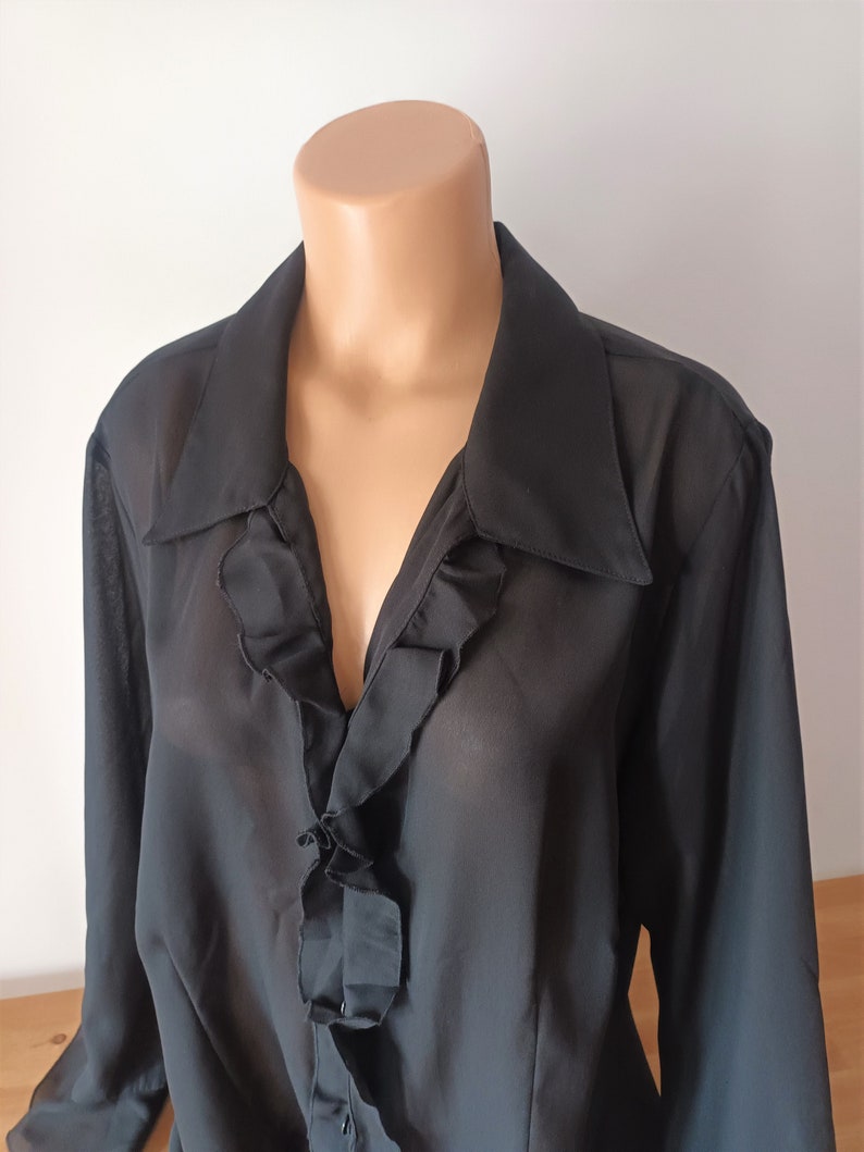 May include: A black sheer blouse with a ruffled neckline and long sleeves.