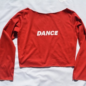 May include: Red long-sleeved crop top with the word "DANCE" printed in white on the front.