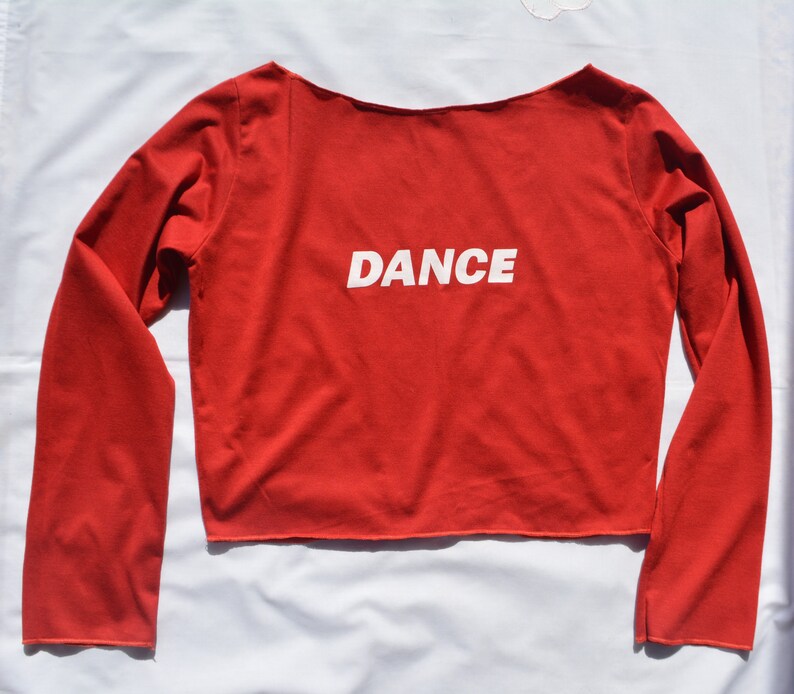 May include: Red long-sleeved crop top with the word "DANCE" printed in white on the front.