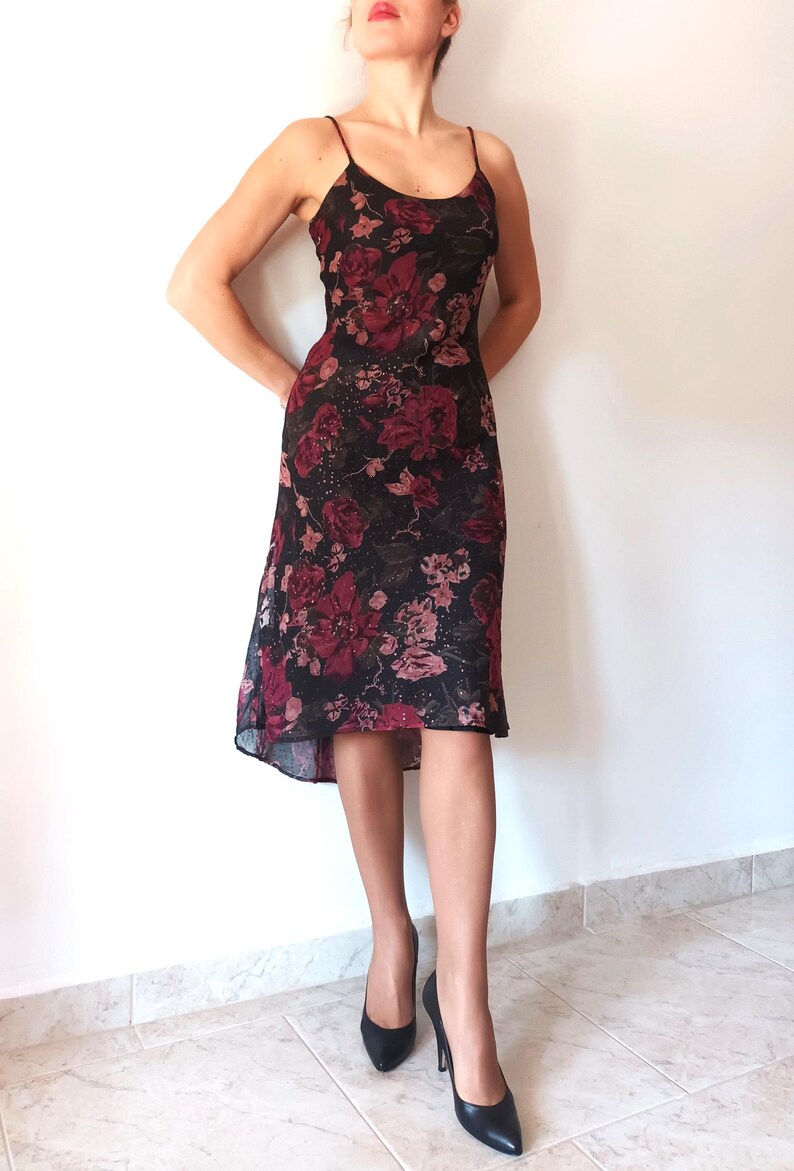 Peut inclure: Une robe midi noire &agrave; imprim&eacute; floral avec des roses rouges et roses. La robe a un corsage ajust&eacute; et une jupe fluide.