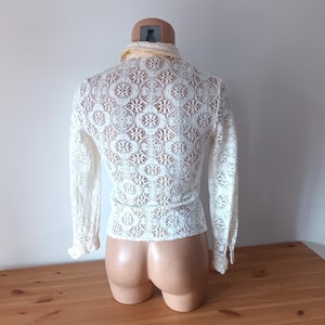 May include: White crochet top with long sleeves and a high collar. The top has a delicate floral pattern.