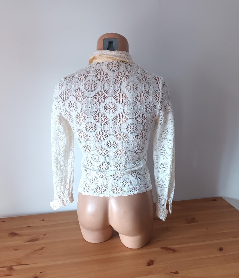May include: White crochet top with long sleeves and a high collar. The top has a delicate floral pattern.