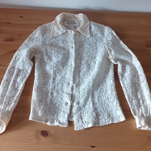 May include: A white lace blouse with long sleeves and a button-up front.