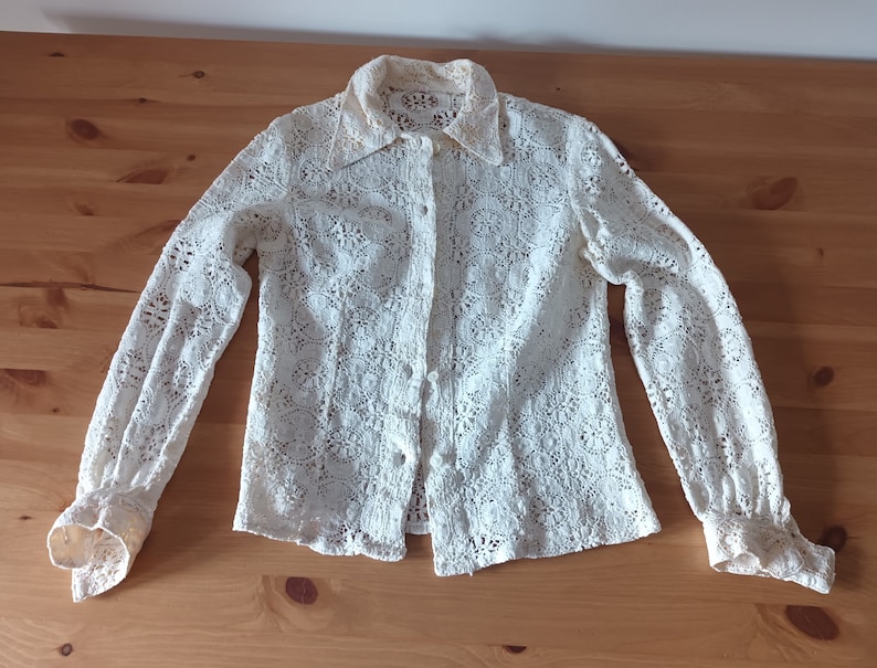 May include: A white lace blouse with long sleeves and a button-up front.