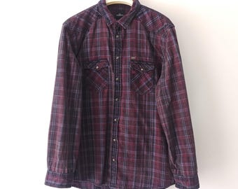 May include: A long-sleeved plaid shirt in shades of burgundy and black. The shirt has a button-down collar, two chest pockets with button closures, and a single button cuff on each sleeve.