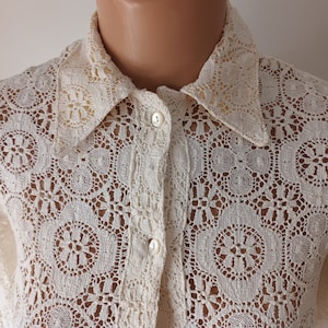 May include: A white crochet button-up shirt with a delicate floral pattern. The shirt has a classic collar and long sleeves.