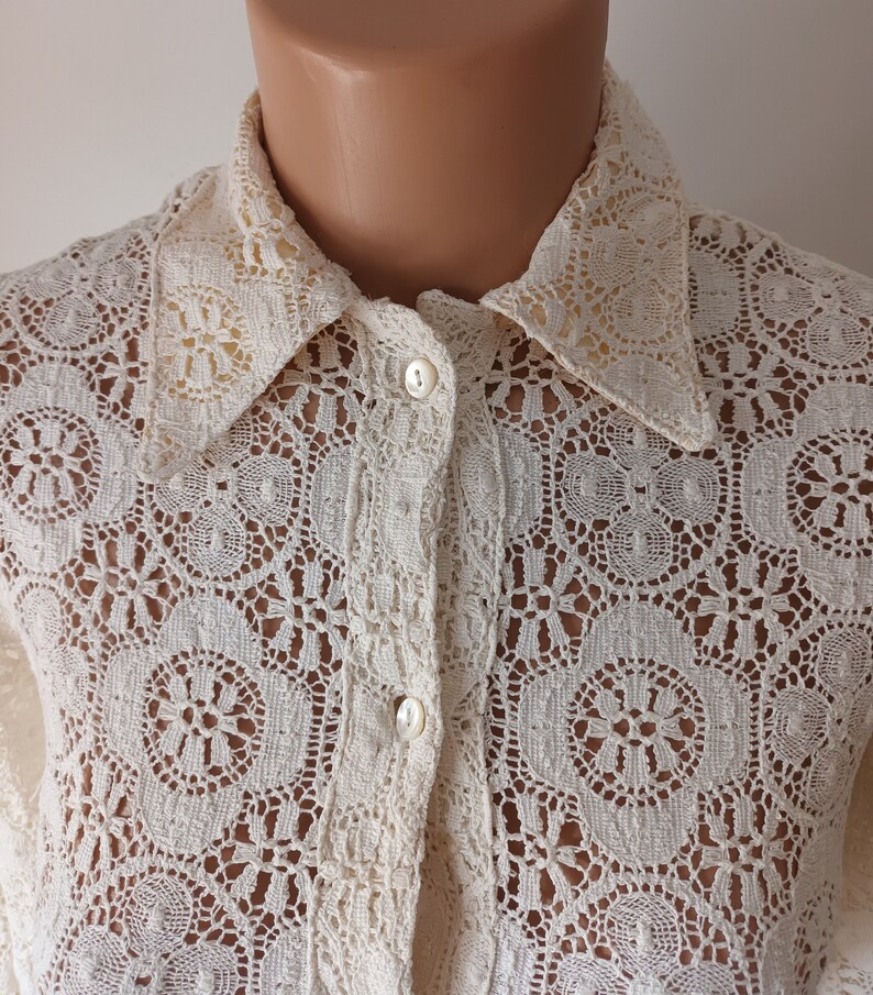 May include: A white crochet button-up shirt with a delicate floral pattern. The shirt has a classic collar and long sleeves.