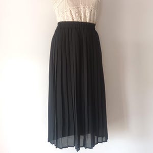 May include: A black pleated midi skirt made of a sheer fabric. The skirt has a high waist and falls to just below the knee.
