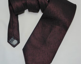 May include: A dark burgundy silk tie with a geometric pattern. The tie is folded and tied in a knot.