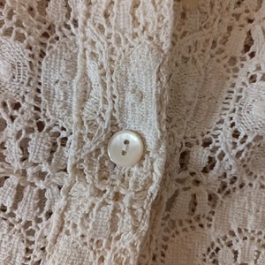 May include: Close-up of a white crocheted fabric with a white button.