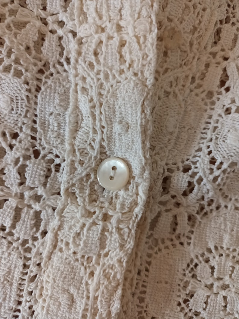 May include: Close-up of a white crocheted fabric with a white button.