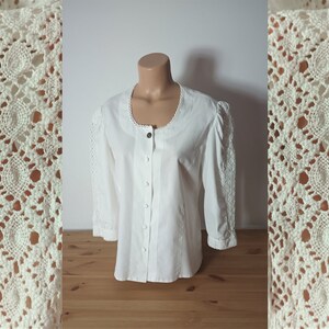 May include: White button-up blouse with a round neckline and long sleeves. The sleeves have a delicate lace trim.