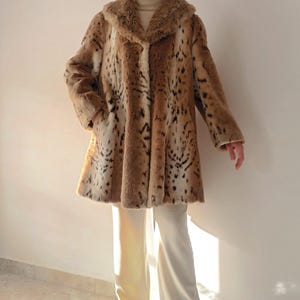 Pode incluir: Um casaco de pele sintética marrom e branco com uma gola grande. O casaco tem um padrão de leopardo.