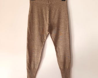 Op de afbeelding: Een paar bruine gebreide broek met een geribbelde boord aan de onderkant van elk been.