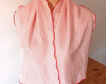 Peut inclure: Écharpe blanche à motif quadrillé rouge et bordure rouge festonnée, drapée sur un mannequin. Le foulard est en tissu léger et a un aspect doux et fluide. L'écharpe est présentée sur une surface en bois.