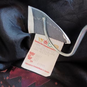 Peut inclure: Une &eacute;tiquette de v&ecirc;tement noire avec du texte blanc d&eacute;taillant la composition du tissu et les instructions d'entretien. L'&eacute;tiquette indique "Gamiture Non Comprise/Exclusive", "100% Polyester", "Lining/Doublure 100% Acetate", "Modele 2827", "Style 731", "Lot 063", "Size CA 01595", et "Fabriqu&eacute; au Canada/Made in Canada".