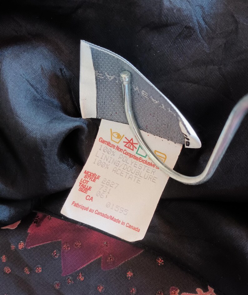 Peut inclure: Une &eacute;tiquette de v&ecirc;tement noire avec du texte blanc d&eacute;taillant la composition du tissu et les instructions d'entretien. L'&eacute;tiquette indique "Gamiture Non Comprise/Exclusive", "100% Polyester", "Lining/Doublure 100% Acetate", "Modele 2827", "Style 731", "Lot 063", "Size CA 01595", et "Fabriqu&eacute; au Canada/Made in Canada".