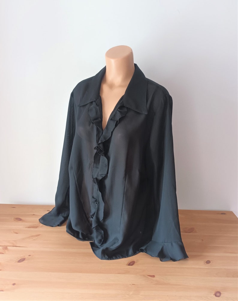 May include: A black sheer blouse with a ruffled collar and long sleeves.