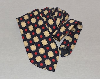 May include: A silk tie with a geometric pattern of red circles and black and white squares on a beige background.