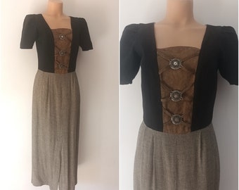 Puede incluir: Un vestido midi negro y marrón con escote cuadrado y mangas cortas. El corpiño presenta un panel de gamuza marrón con botones plateados decorativos. La falda es de cuadros marrones y blancos.