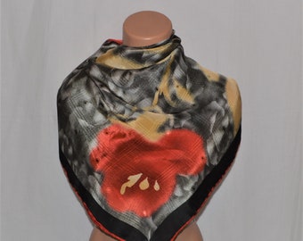 Puede incluir: Un pañuelo de seda con estampado negro, dorado y rojo con un gran diseño de flor roja. El pañuelo tiene un borde negro.