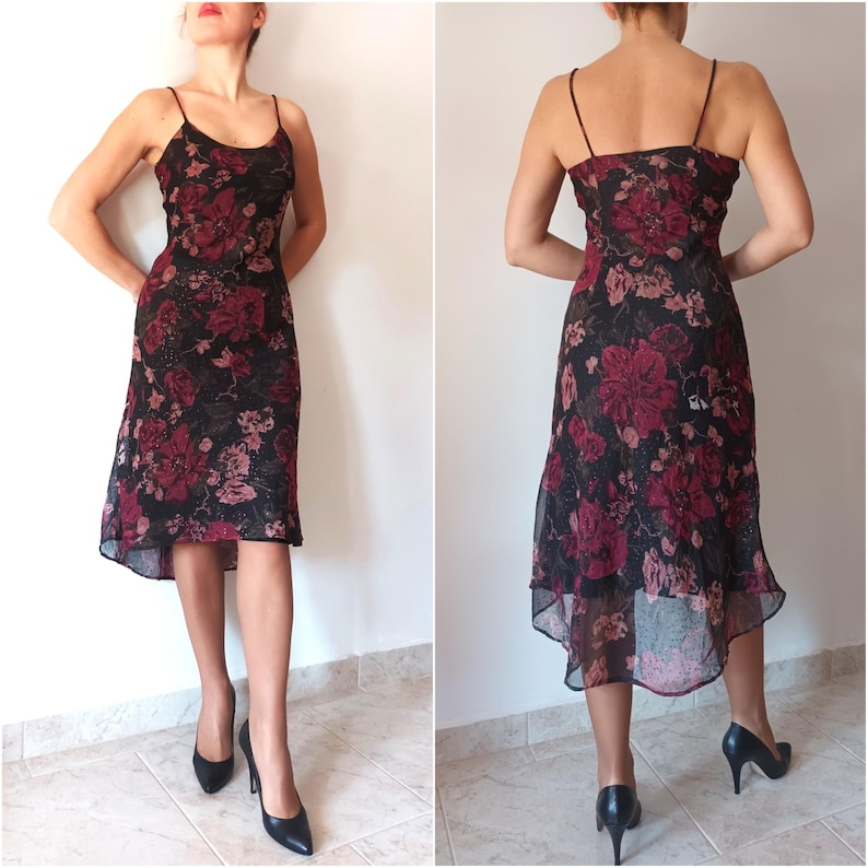 Peut inclure: Une robe midi &agrave; imprim&eacute; floral noir et rouge avec une jupe asym&eacute;trique et des bretelles spaghetti. La robe est en tissu transparent et a un corsage ajust&eacute;.