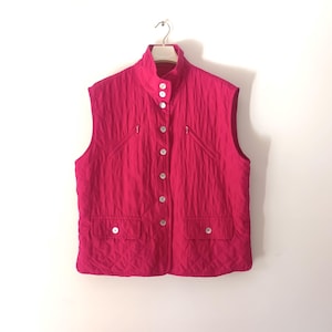May include: A quilted vest in a bright pink color with a button-up front and two zippered pockets. The vest has a high collar and is sleeveless.