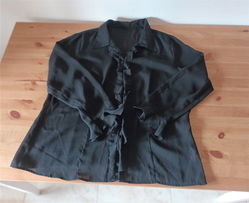 May include: A black sheer blouse with a ruffled neckline and long sleeves. The blouse has a button-up front and a tie at the waist.