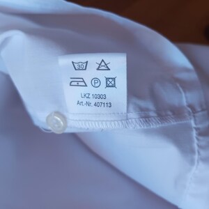 Pode incluir: Uma camisa branca com uma etiqueta de cuidados contendo s&iacute;mbolos de lavagem, incluindo um &iacute;cone de lavagem a 30 graus, um s&iacute;mbolo de n&atilde;o usar lix&iacute;via, um &iacute;cone de ferro, um s&iacute;mbolo de limpeza a seco e um s&iacute;mbolo de secadora. LKZ 10303 e Art.-Nr. 407113.
