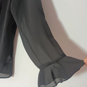 May include: Black sheer blouse with long sleeves and a ruffled cuff detail.