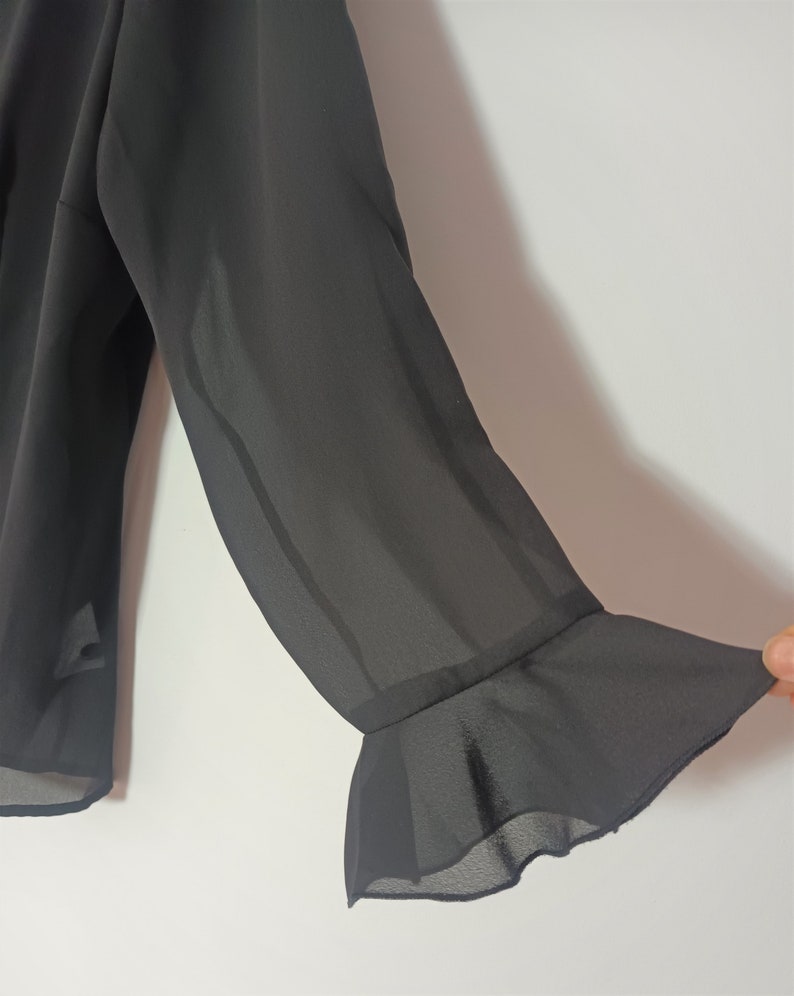 May include: Black sheer blouse with long sleeves and a ruffled cuff detail.