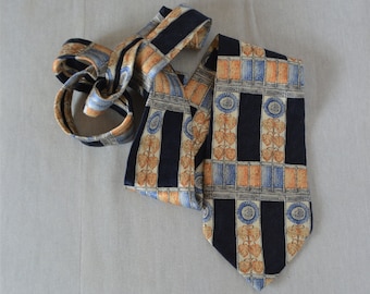 Puede incluir: Una corbata de seda azul marino con un patrón geométrico de naranja, azul y blanco. El patrón presenta hojas estilizadas y círculos.
