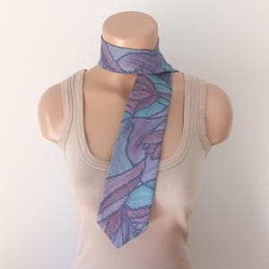 May include: A purple and blue patterned tie with a floral design. The tie is on a mannequin wearing a beige tank top.