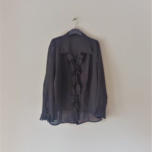 May include: A black sheer blouse with a ruffled neckline and long sleeves.