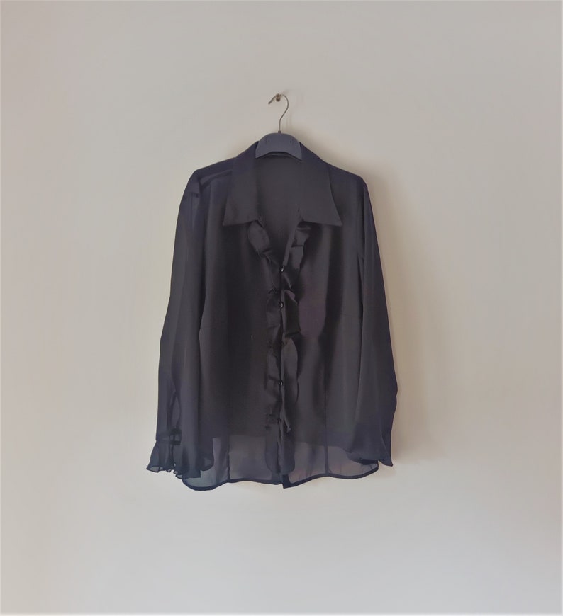 May include: A black sheer blouse with a ruffled neckline and long sleeves.