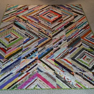 Może przedstawiać: Kolorowy koc wykonany z pasków tkaniny zszytych w kształt rombu. Koc składa się z wielu różnych kolorów i wzorów, w tym czerwonego, niebieskiego, zielonego, żółtego i fioletowego. Koc jest obszyty zieloną tkaniną.