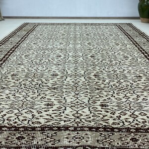 May include: A vintage style rug with a cream background and a brown floral pattern. The rug has a brown border with a geometric design.