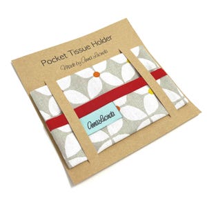 May include: A floral pocket tissue holder in grey and white, with a red band, presented on a brown card. The card reads "Pocket Tissue Holder" and "Made by Anna Lucinda".