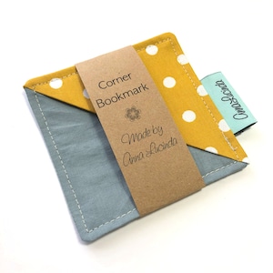May include: A yellow and blue fabric corner bookmark with white polka dots. The bookmark has a brown paper tag that says "Corner Bookmark" and "Made by Anna Lucinda".