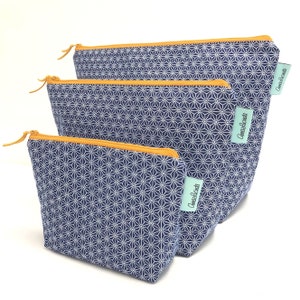 May include: Three navy blue zippered pouches with a white geometric star pattern. Each pouch has a gold-coloured zip and a small, rectangular tag with text. The pouches are in different sizes.