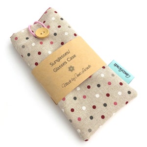 May include: A beige fabric sunglasses or glasses case with red, white, and gray polka dots. The case has a pink elastic band and a brown paper label that reads "Sunglasses/Glasses Case Made by Anna Lucinda".