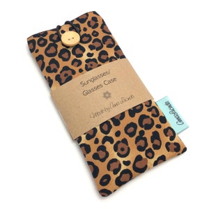 May include: A leopard print glasses case with a wooden button closure. The case has a brown paper label that says "Sunglasses/Glasses Case" and "Made by Anna Lucinda".