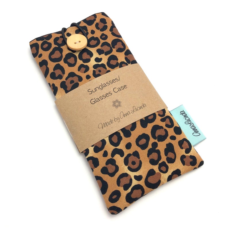 May include: A leopard print glasses case with a wooden button closure. The case has a brown paper label that says "Sunglasses/Glasses Case" and "Made by Anna Lucinda".