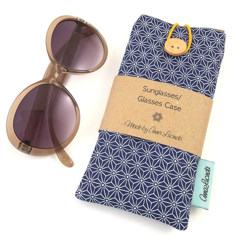 May include: A blue and white patterned fabric sunglasses case with a brown label that reads "Sunglasses/Glasses Case Made by Anna Lucinda".