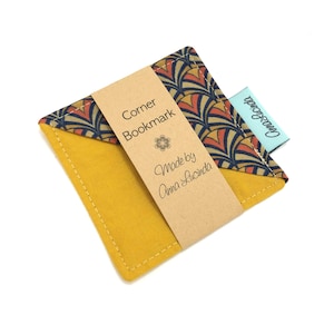 May include: A yellow fabric corner bookmark with a patterned fabric flap. The bookmark has a brown paper label that reads "Corner Bookmark" and "Made by Anna Lucinda".