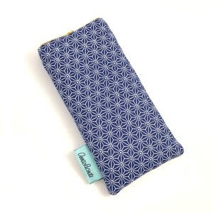 May include: A blue and white patterned eye mask with a mustard yellow lining. The eye mask has a small blue label with the text "Cuna & Lecrina" on it.